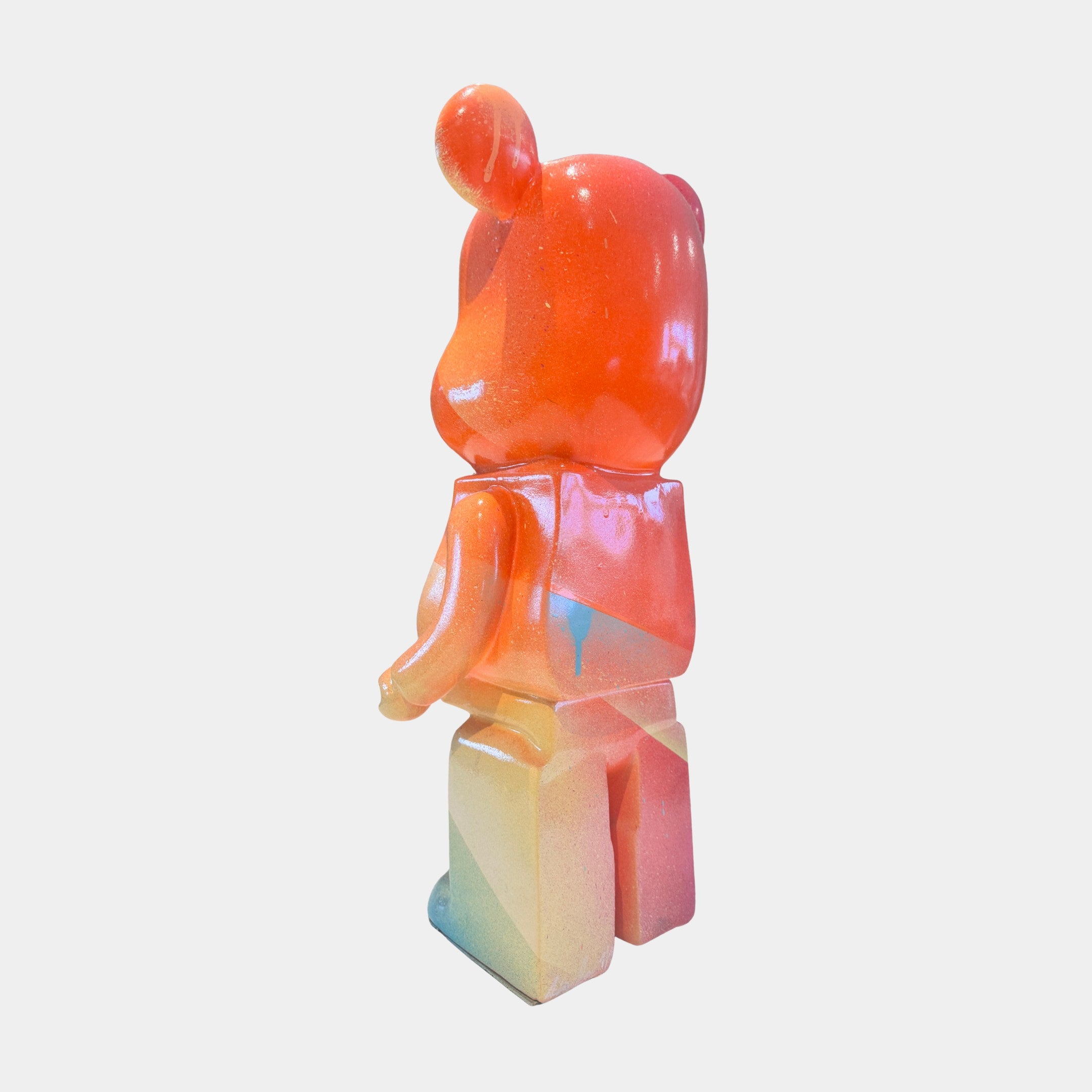 The Candy Bear Sculpture - 165cm by Giant Sculptures stands facing away, painted with a glossy gradient of orange, red, yellow, blue, and purple on a plain white background—a playful contemporary art piece.