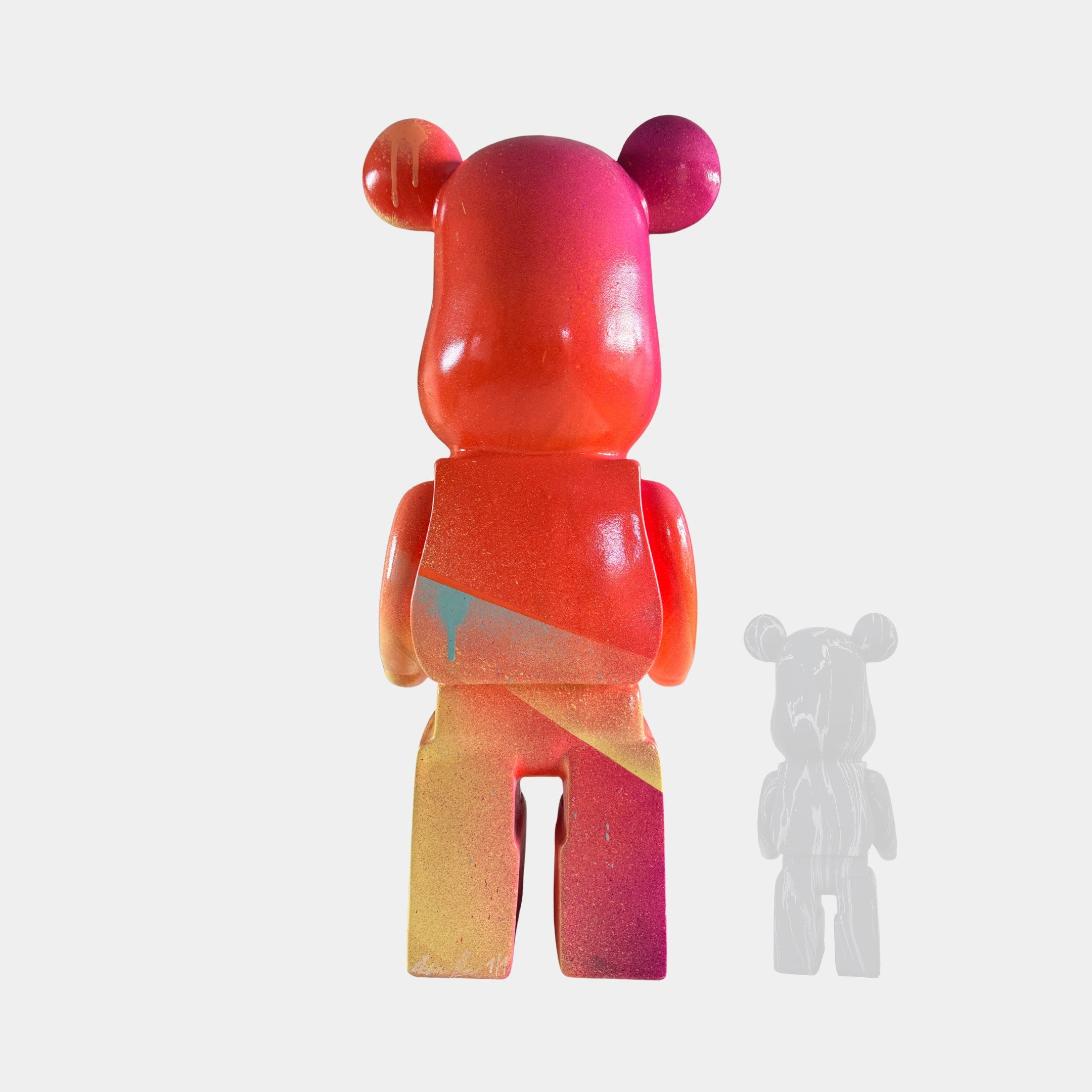 The Candy Bear Sculpture - 165cm by Giant Sculptures features a vibrant red, pink, orange, and yellow gradient. Shown from the back with a smaller semi-transparent gray version to the right, it stands out against a white background.
