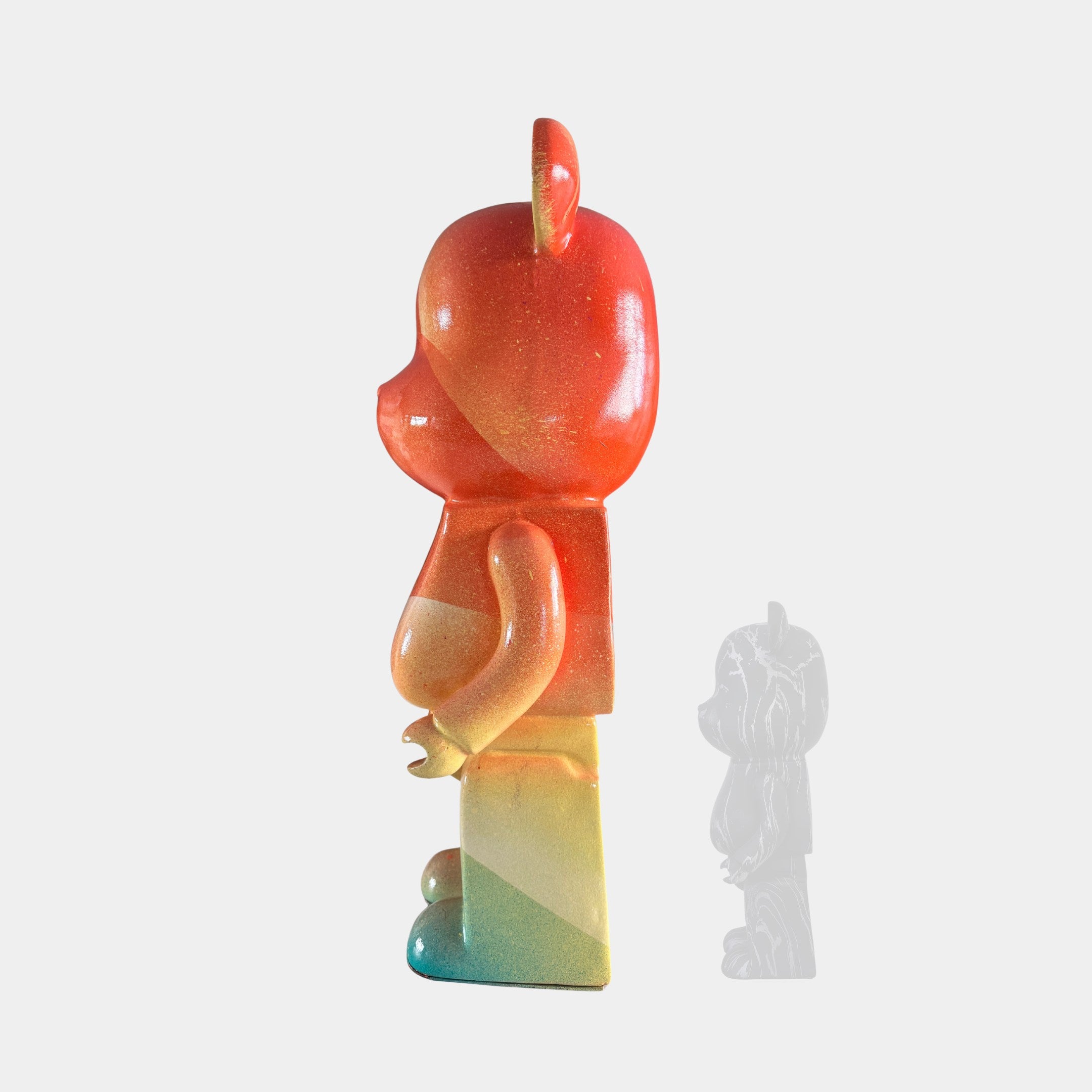 The Candy Bear Sculpture - 50cm by Giant Sculptures features a vibrant bear-shaped figurine with red, orange, yellow, and blue hues in profile. A smaller translucent version accompanies it—an eye-catching limited edition art piece.
