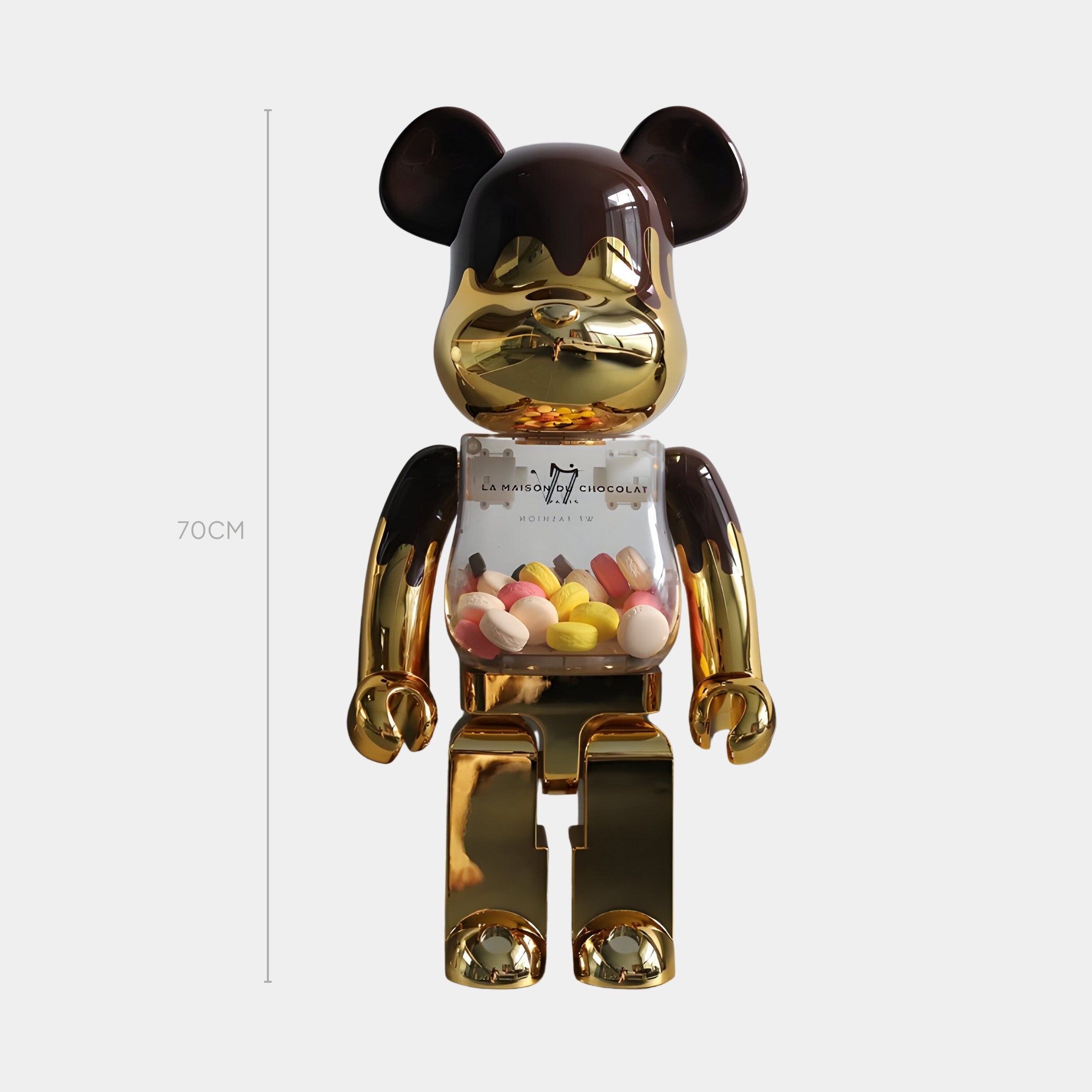 The 70cm Chocolate Drip Bear Sculpture by Giant Sculptures in mirror gold and black, with a transparent chest filled with colorful candies, stands upright against a plain light background.