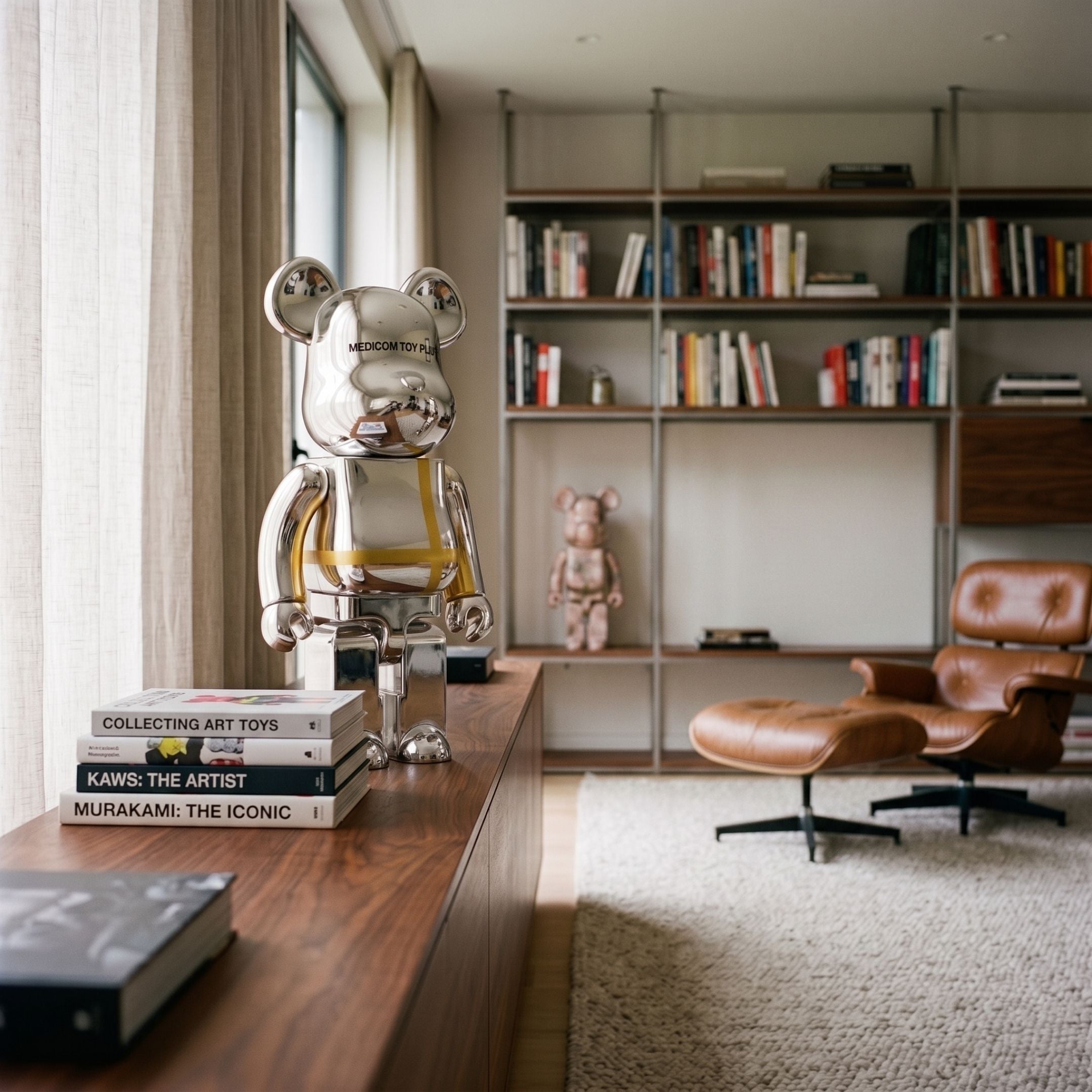 Atelier Chrome Grid Bear Sculpture, 70cm, mirror-chrome finish with yellow grid detailing, displayed on a wooden sideboard beside books in a living room with a bookshelf and leather lounge chair.
