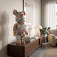 Comic Wonder Bear Sculpture - 70cm, a multicoloured pop-art bear figure covered in cartoon and floral motifs, displayed on a wooden sideboard in a living room.