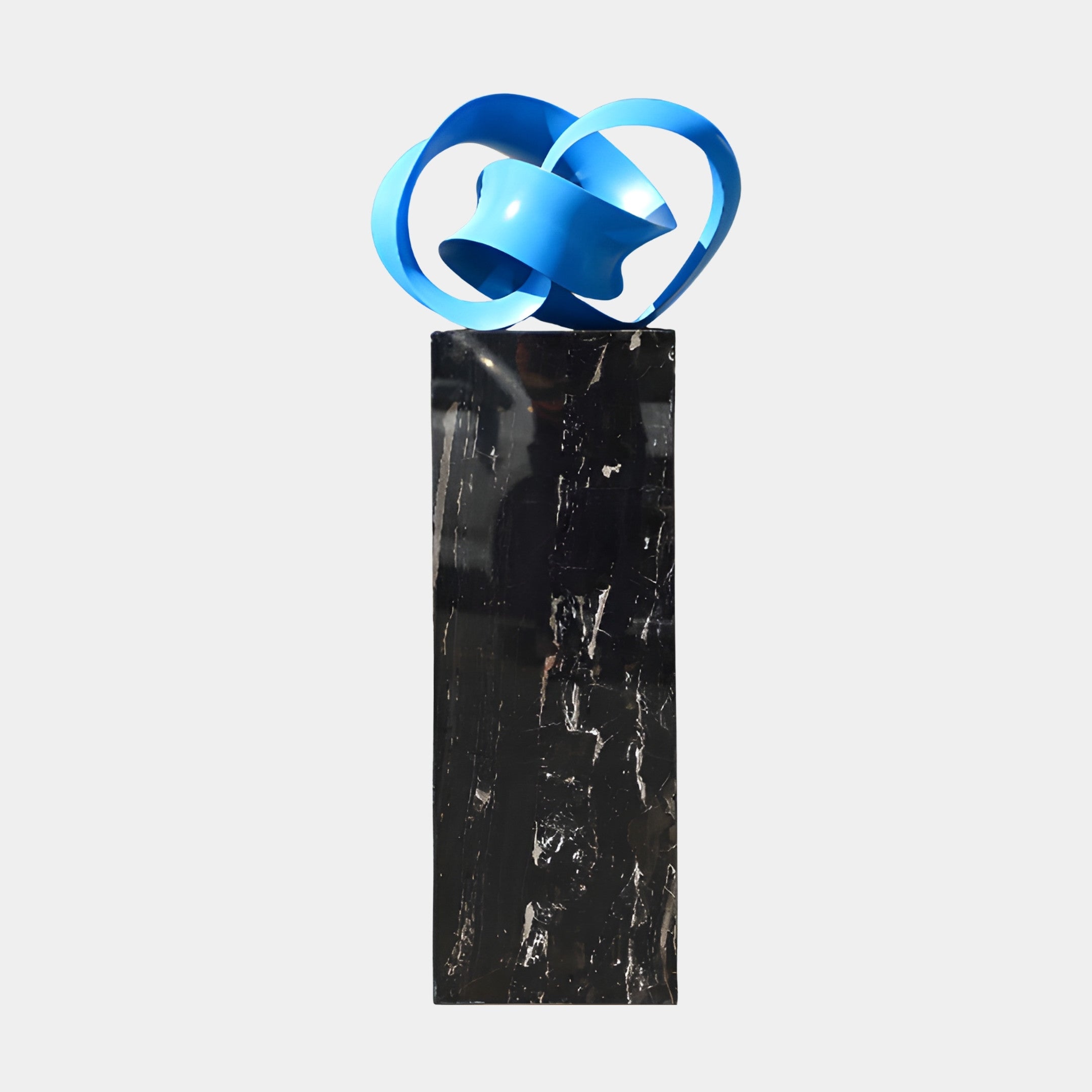 Glossy blue 3D-printed resin infinity knot sculpture by Giant Sculptures, displayed on a tall black marble plinth against a plain light background.