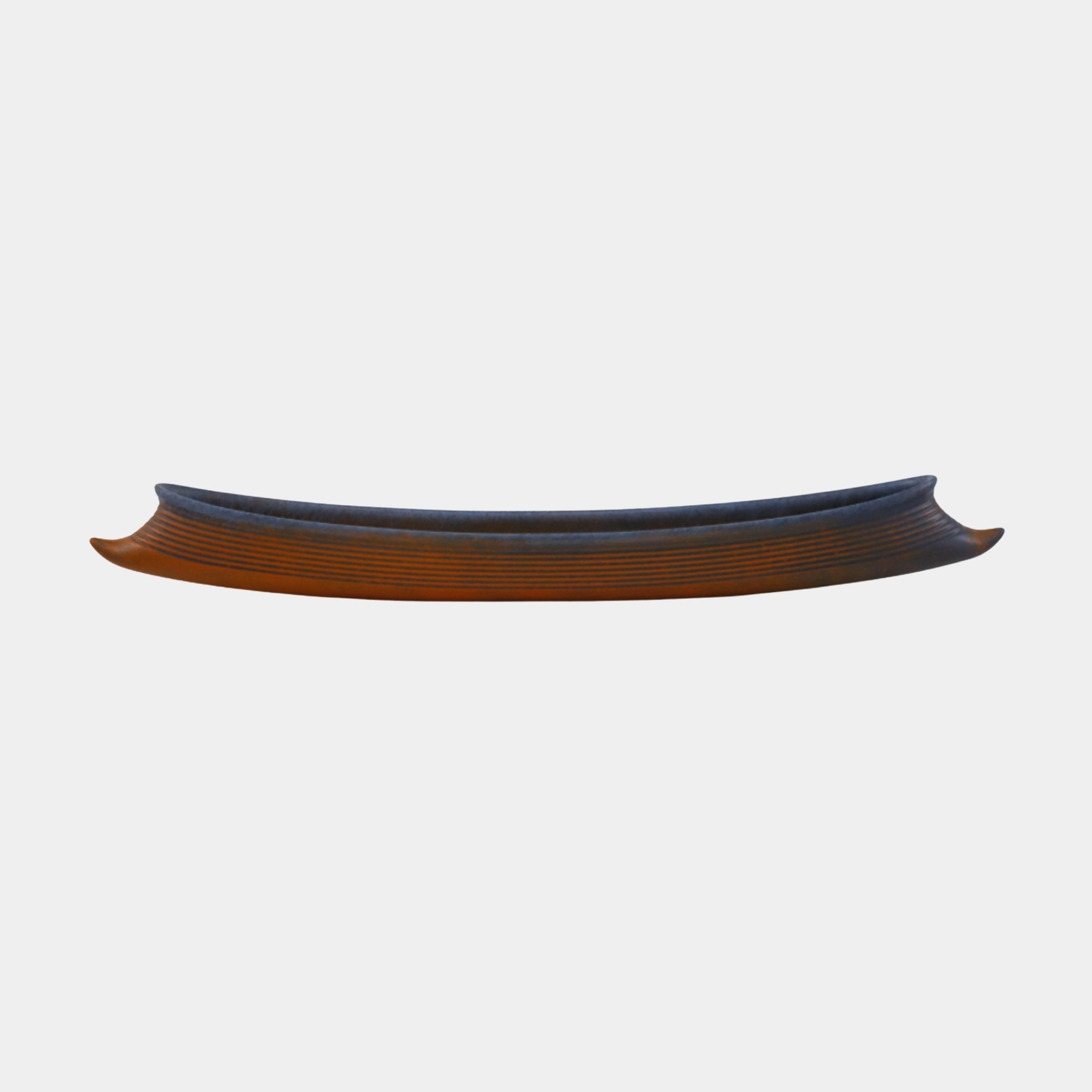 Side view of the Giant Sculptures Terracotta Ribbed Boat Bowl Sculpture 44cm, showing its long curved form, ribbed orange exterior, and dark blue interior.
