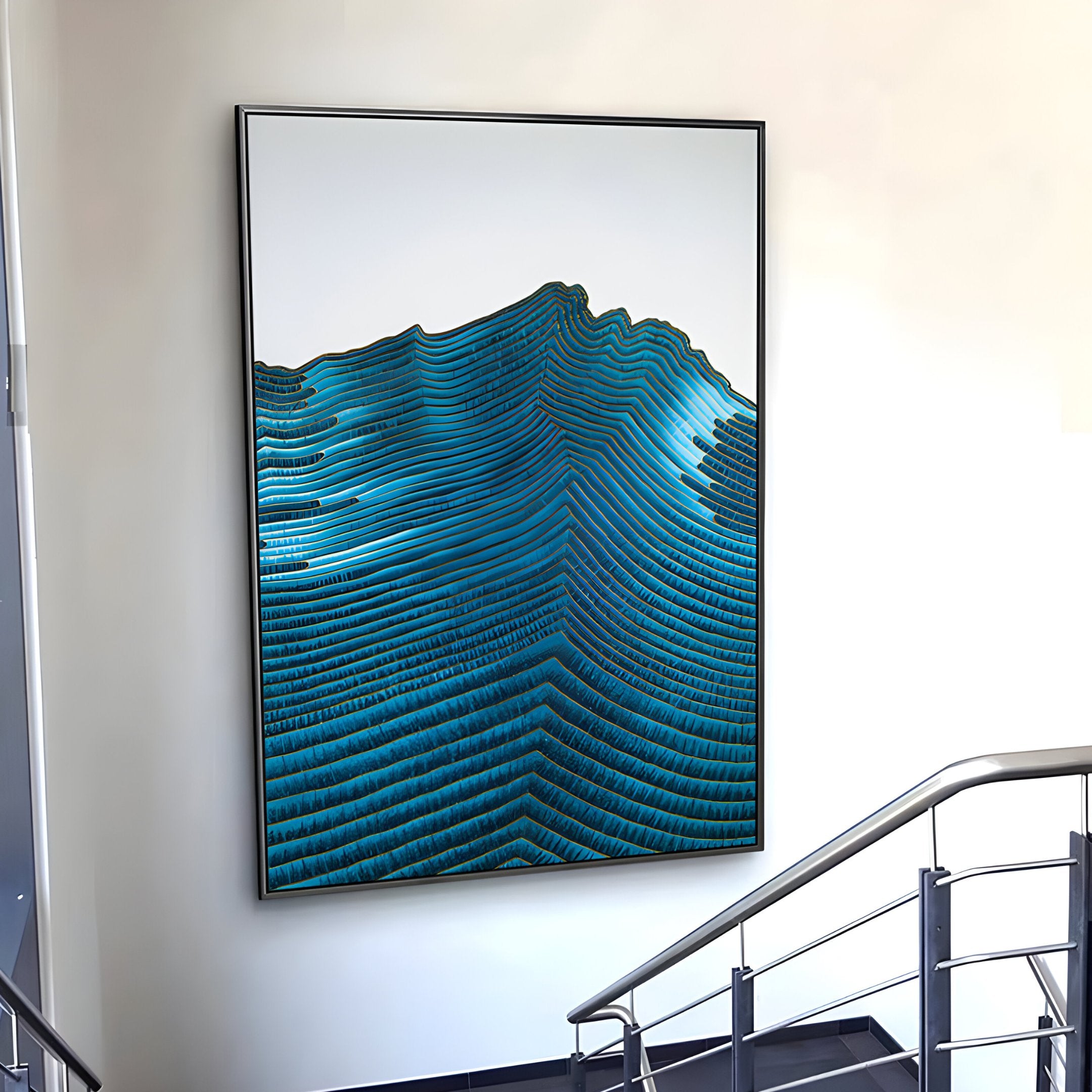 Giant Sculptures Ripplewave III Abstract Blue Decorative Enamel Wall Art features wavy blue and teal lines like topographic patterns, enhancing the white wall by the staircase. It sits in a sleek modern frame, perfectly complemented by a silver handrail in this contemporary setting.