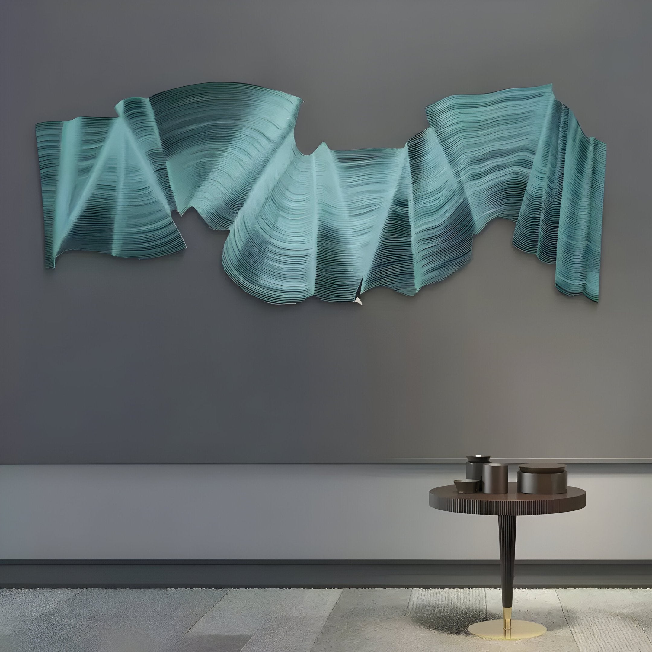 The Giant Sculptures Rollscape Aqua Cascade Enamel Wall Art features an abstract, blue-green metal with folded, wave-like shapes on a gray backdrop. Below is a round black table with a gold base and an enamel item on a textured floor.