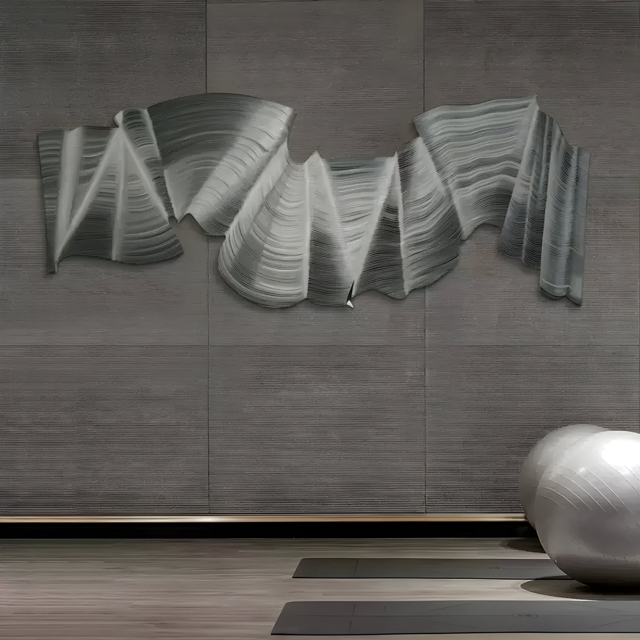 A chic interior highlights Giant Sculptures Rollscape Grey Flow Enamel Decorative Wall Art on a gray wall, mimicking flowing fabric. Below, two yoga mats and a large silver exercise ball rest on the wooden floor, crafting a minimalist and serene setting ideal for luxury interiors.