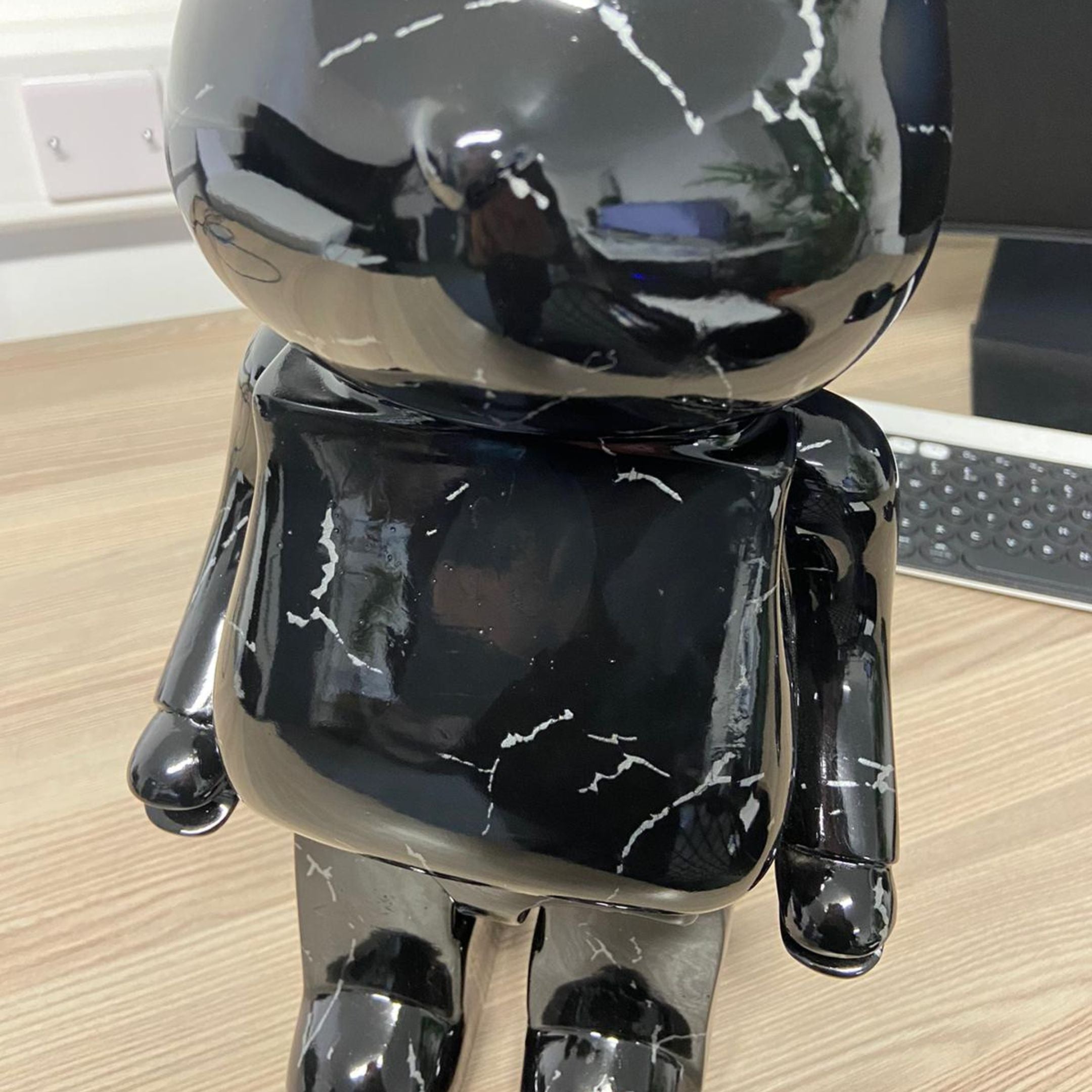 Black Stone Bear Sculpture 50cm by Giant Sculptures with glossy water-transferred marbled finish, displayed on a wooden desk beside a keyboard and monitor.