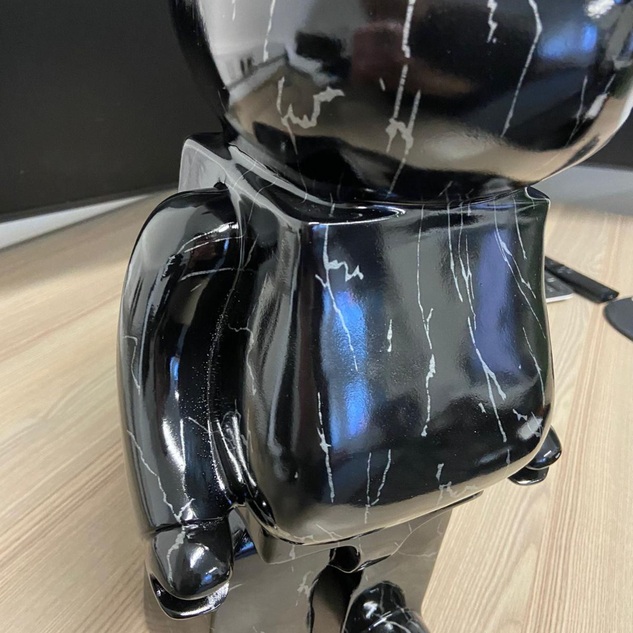 Close-up of the Giant Sculptures Black Stone Bear Sculpture 50cm, showing the glossy black resin body with white marbled veining on a wood floor.