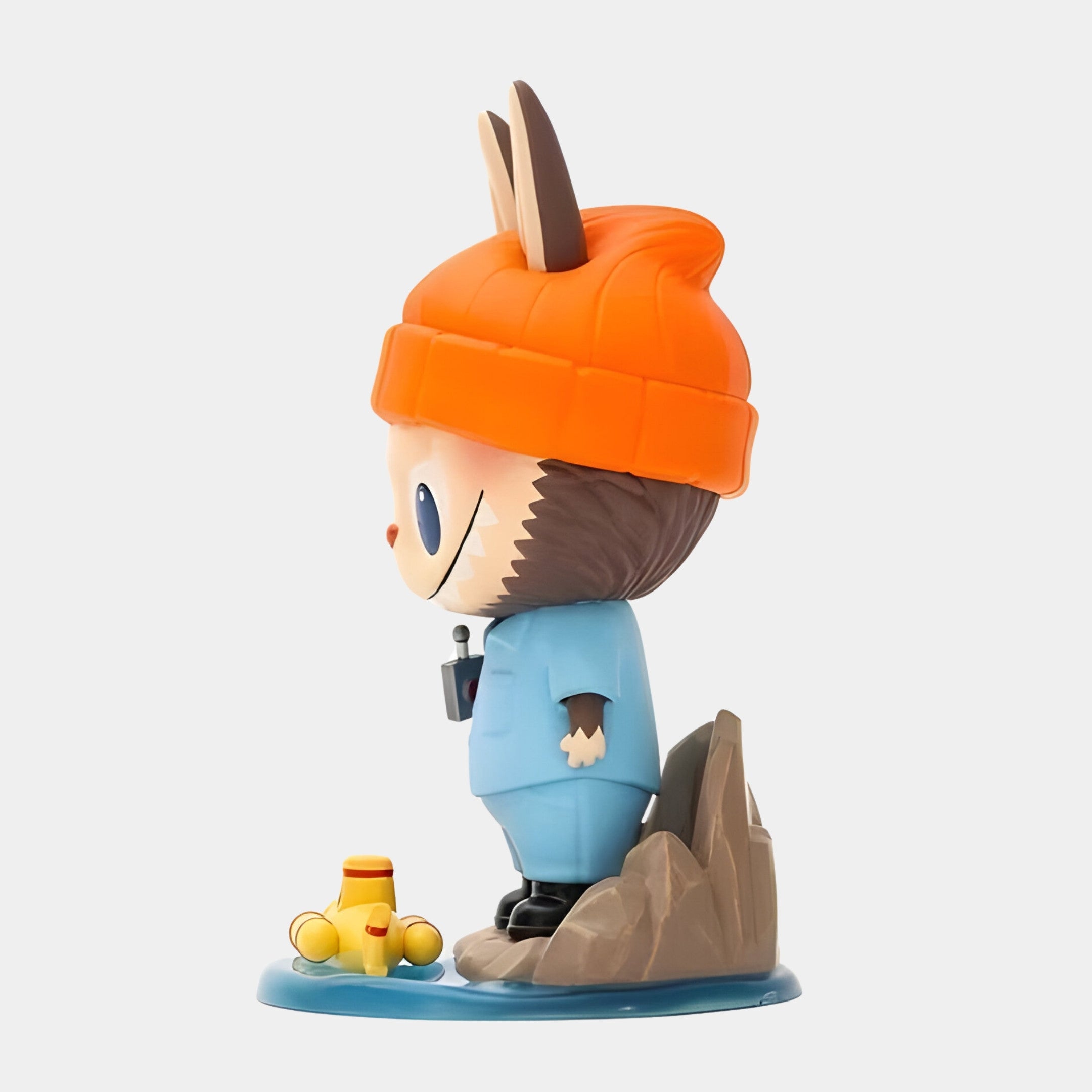 The Submarine Explorer Labubu Sculpture - 100cm by Giant Sculptures features a cartoonish animal in a blue outfit and orange hat, standing on a rocky base with a yellow submarine toy—an eye-catching collectible for any space.