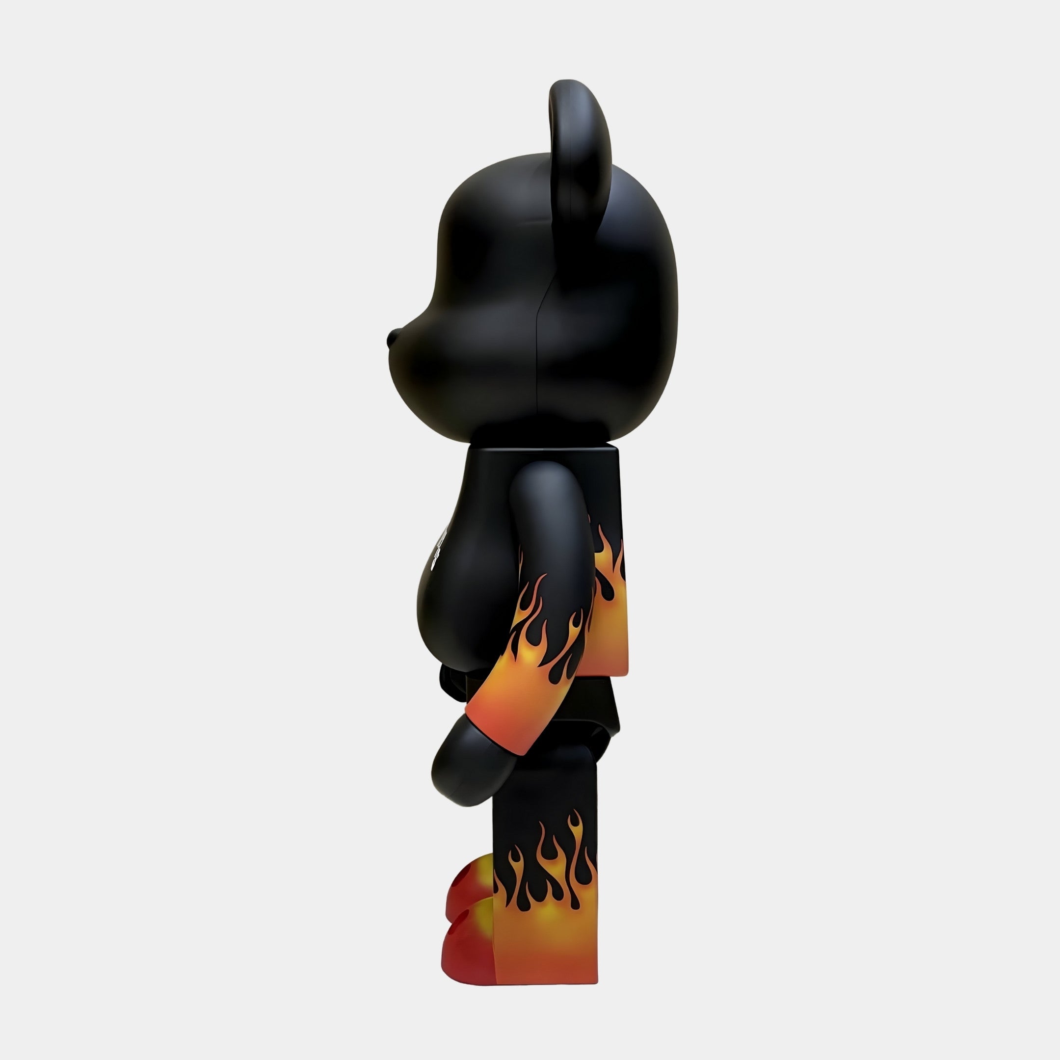 The Flame Black Bear Sculpture - 70cm by Giant Sculptures features gradient orange and yellow flames on its arms, legs, and lower torso, with red feet for a bold accent. The bear stands in profile view facing left.