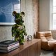 Forest Drift Bear Sculpture - 70cm in green, brown, and black camouflage resin, displayed on a wooden credenza beside books and a clock in a modern living room.