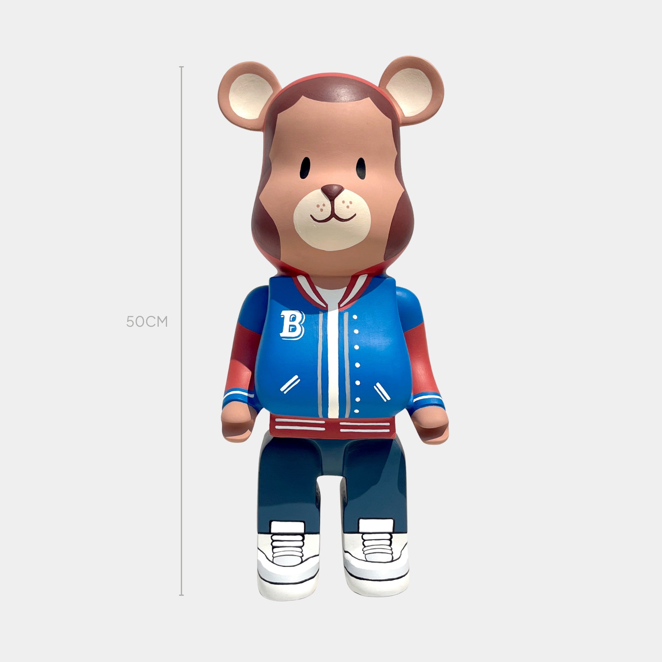 The Giant Sculptures Fresh Grizz Bear Sculpture - 50cm features a bear in a blue and red varsity jacket with a B, navy pants, and white sneakers—a striking streetwear-inspired collectible set against a light gray backdrop.