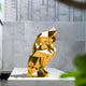 Displayed on a white platform outdoors, the Contemplative Gold Geometric Steel Sculpture (130cm) by Giant Sculptures stands against a textured gray wall, with green leaves peeking through in the foreground.