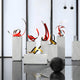 A modern art gallery showcases contemporary abstract metal sculptures in shades of red and yellow, featuring the eye-catching Ribbon Red V Abstract Steel Sculpture by Giant Sculptures, which boasts a ribbon design and stands at 59cm. These vibrant pieces are displayed on white pedestals, with their colors popping against a minimalistic backdrop highlighted by a sleek black floor. In the foreground, a large black sphere completes the scene.