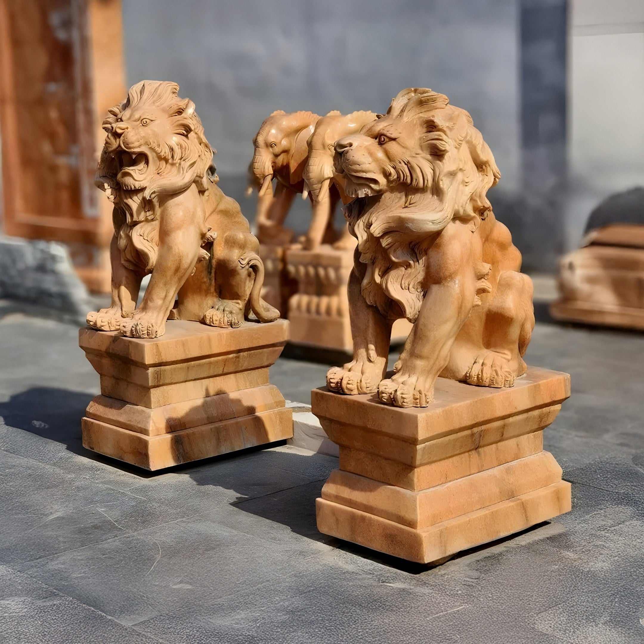 The Giant Lion Yellow Marble Outdoor Sculptures by Giant Sculptures, measuring 120cm, feature intricately detailed lions with flowing manes and fierce expressions, set on matching pedestals in sunlight. These majestic sculptures enhance any paved area with style.