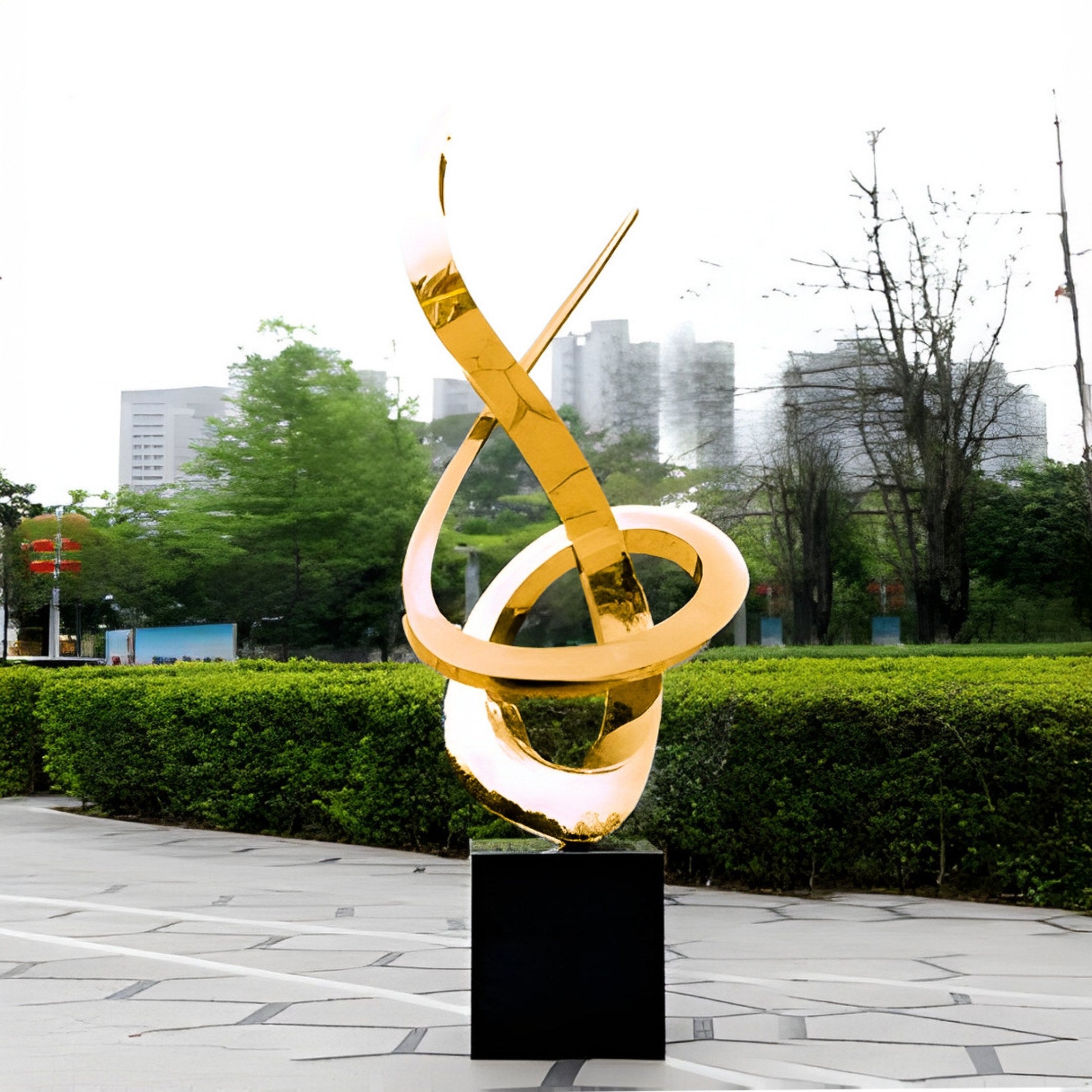 The Echo Gold Abstract Steel Outdoor Sculpture by Giant Sculptures, measuring 250cm, features modern twisting loops on a black pedestal against hedges, trees, and blurred buildings in a cloudy sky—a testament to modern arts captivating allure.