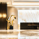 The luxurious hotel lobby features a polished marble floor and the Flow II Gold Organic Steel Sculpture by Giant Sculptures. A textured black wall with ornate lighting contrasts against this, crafting a sophisticated and modern ambiance.