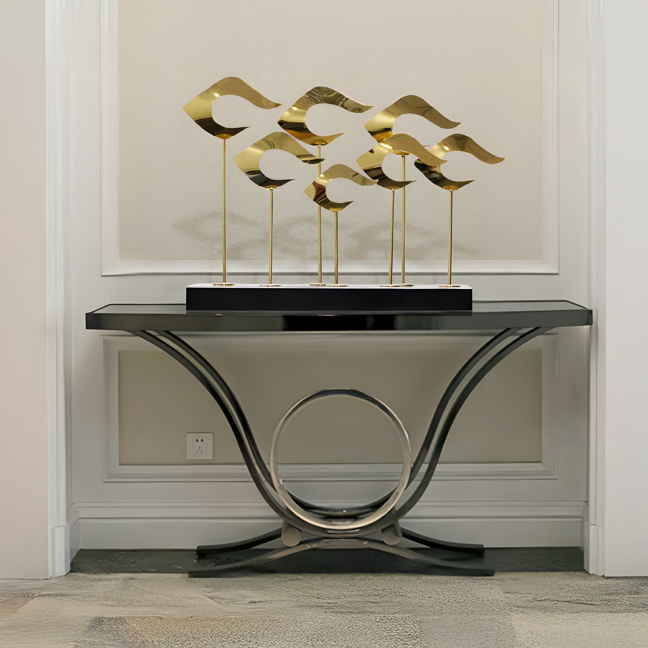 A sleek console table with a metallic circular base and black tabletop exudes sophistication, displaying the Giant Sculptures Golden Drift Abstract Steel Sculpture with wave forms against a light grey paneled wall.