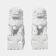 The Chinese Guardian Lion IV Marble Outdoor Sculptures by Giant Sculptures feature two 180cm intricate white marble lions on pedestals. Their detailed curly manes and decorative orbs under their paws enhance the symmetry, with a plain background highlighting these outdoor sculptures.