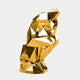 Abstract geometric gold human sculpture, seated with a bent knee, made from polished golden facets, reflecting light and its environment.