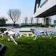 Two geometric stainless steel animal sculptures by Giant Sculptures, featuring the Panther Geometric Steel Outdoor Sculpture - 212cm and its counterpart cheetah, grace the grassy area outside a modern building against a backdrop of trees and clear blue sky.