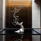 A sleek sculpture from Giant Sculptures, the Magical Antler Steel Outdoor Sculpture - 235cm, features a gracefully elongated neck and antlers resembling tree branches and leaves. It is made of stainless steel and stands elegantly on a reflective black surface in a modern, well-lit room.