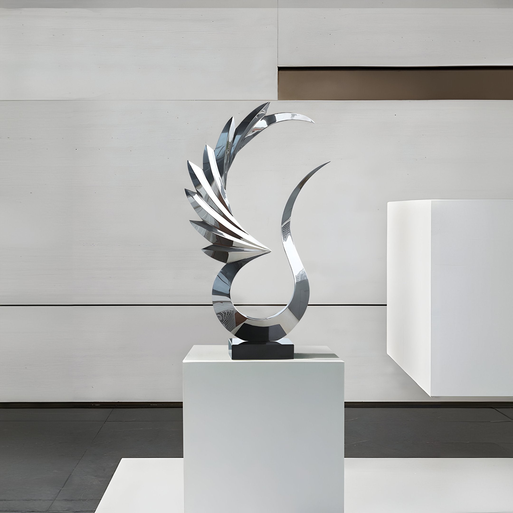 The "Wings Of Light Silver Abstract Steel Sculpture - 102cm" by Giant Sculptures stands proudly on a pedestal in a modern gallery setting. Its sleek, wing-like elements are beautifully complemented by the minimalist gray and white walls and floor, enhancing its reflective surfaces and embodying modern sophistication with contemporary design.