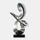 The Serpentine III Silver Abstract Steel Sculpture from Giant Sculptures, measuring 77 cm, showcases a fluid design with intertwined glossy metal loops, elegantly mounted on a black base. This exquisite piece of modern art features a reflective surface that looks dynamic and artistic against a plain backdrop.