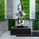 Infinity Arc stainless steel sculpture showcased in a landscaped garden, reflecting light and blending with greenery.