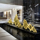 A modern interior space showcases Giant Sculptures Mountain Range Gold Abstract Steel Sculptures on a reflecting pool, surrounded by geometric architecture and a grid-like wall structure, all in a cream and black color scheme.