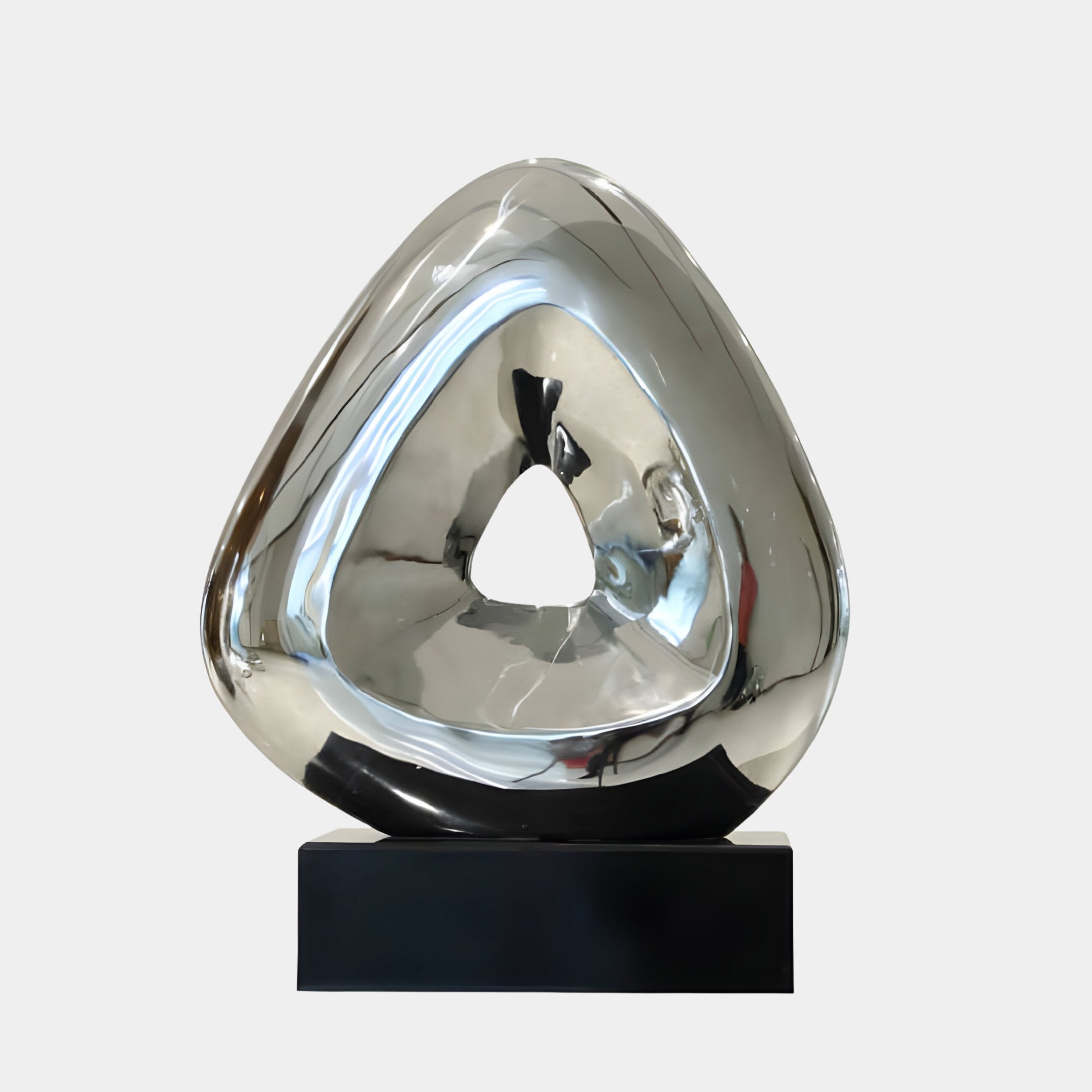 The "Oculus III Abstract Steel Sculpture - 35cm" by Giant Sculptures is a silver, triangular piece created from stainless steel, showcasing a hollow center and resting on a black base. Its reflective surface subtly distorts the shapes and light in its environment.