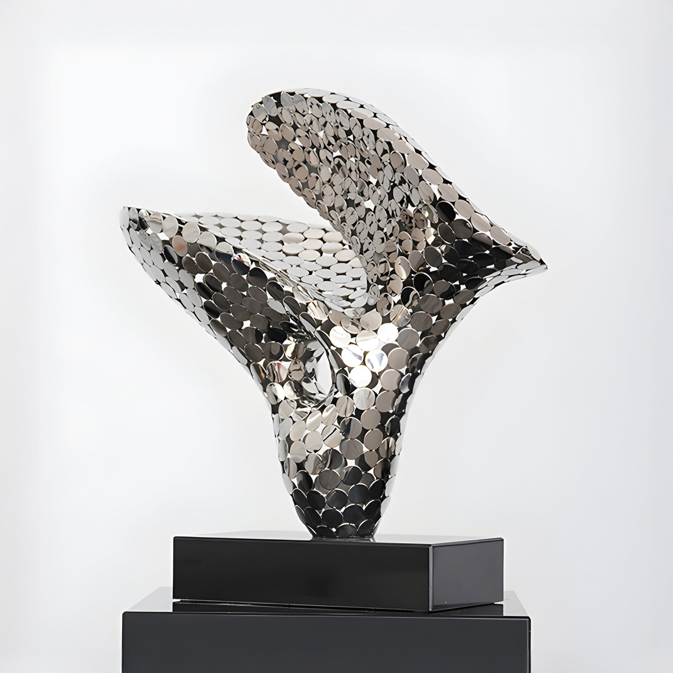 Different angle of the silver sculpture showing its flowing abstract form on a black base.