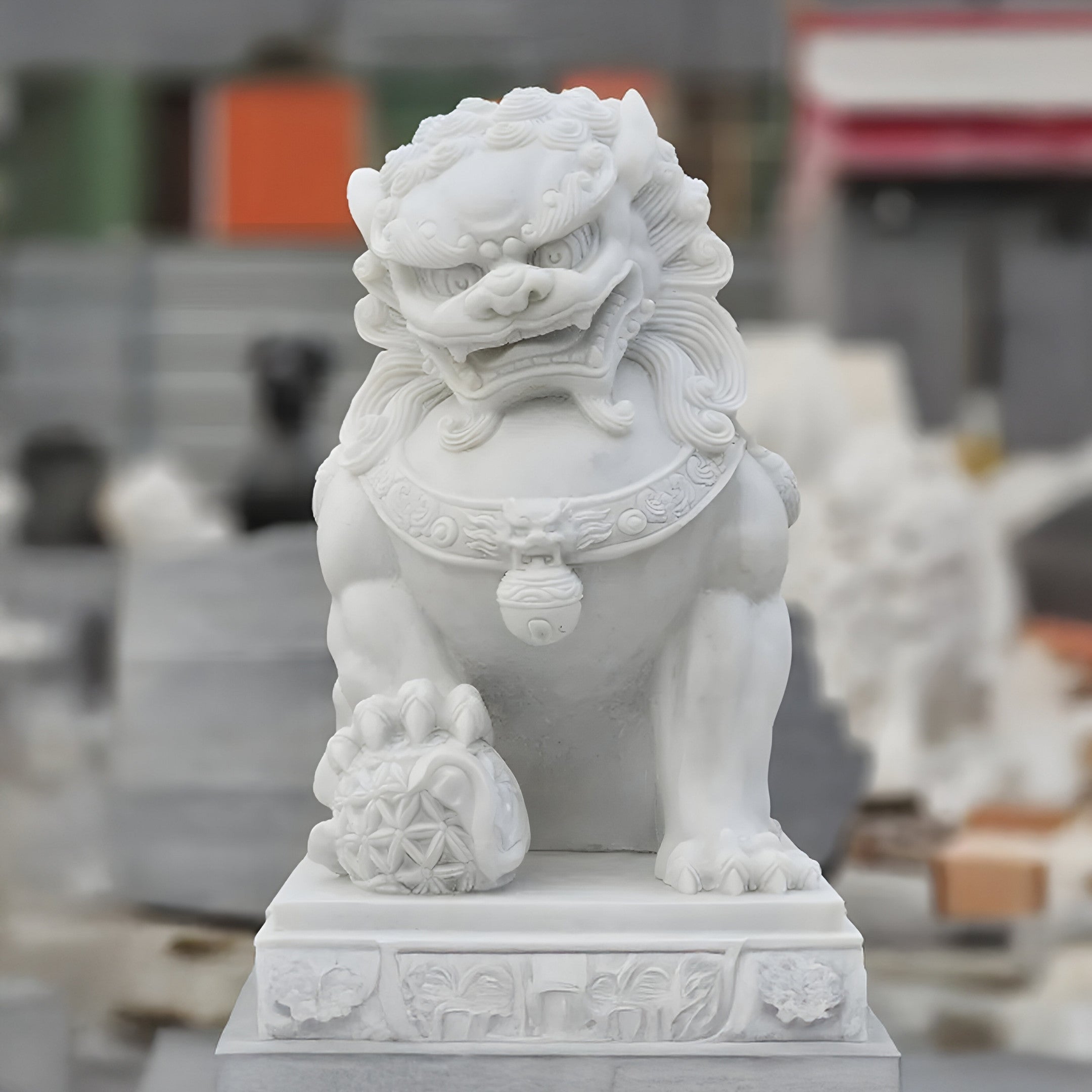 The Giant Sculptures Chinese Guardian Lion Marble Outdoor Sculpture, 150cm tall, depicts a lion with a detailed mane on a rectangular pedestal, holding an ornate orb under its paw. The slightly blurred colorful background enhances this majestic outdoor piece.