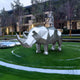 The Rhino Geometric Steel Outdoor Sculpture - 210cm by Giant Sculptures enhances the lawn with its geometric design and circular pathways, while trees and a building in the background are softly illuminated, creating a modern and serene outdoor setting.