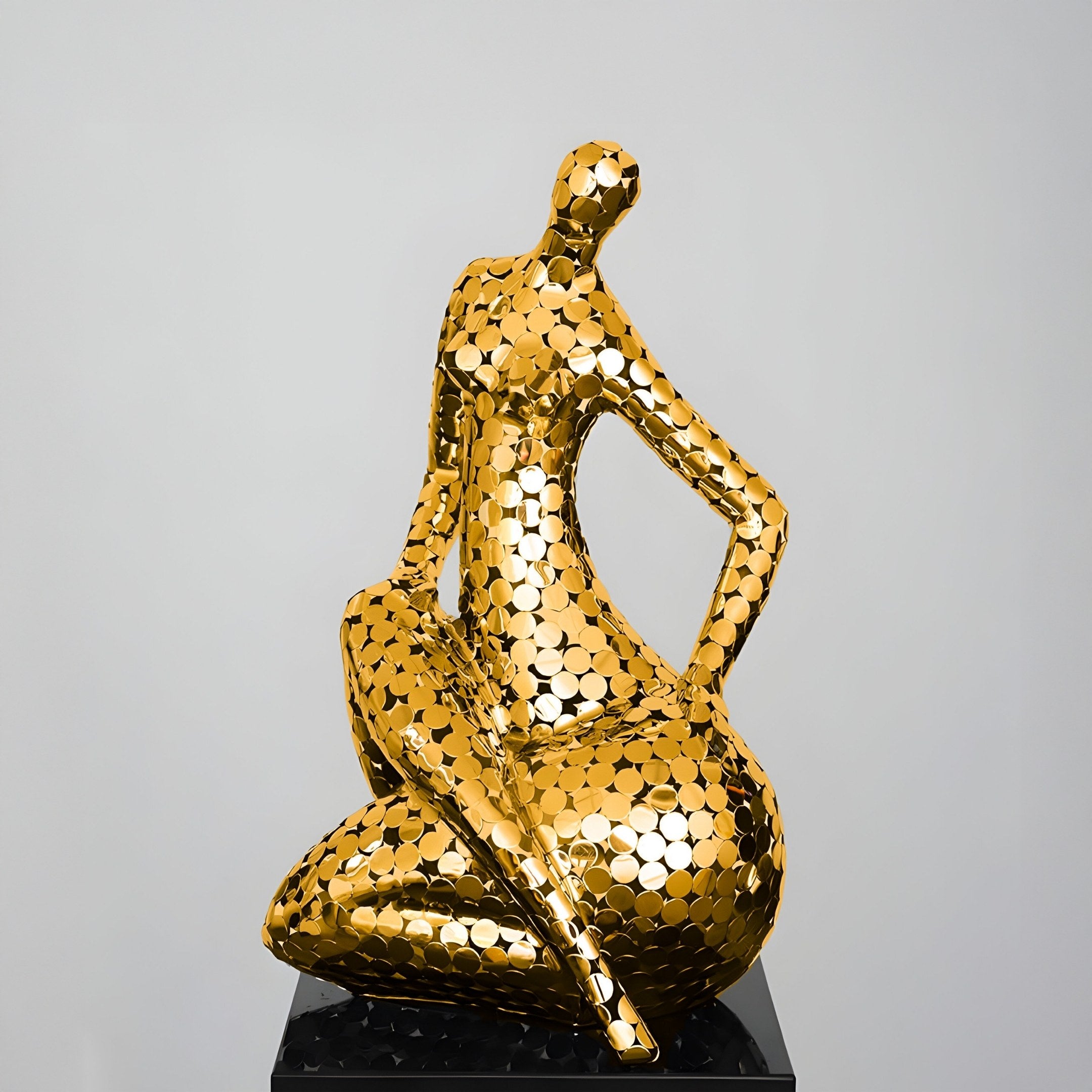 The Solace Gold Abstract Steel Sculpture by Giant Sculptures features a modern seated human figure with reflective gold hexagon details on a black base, exemplifying tranquil luxury and contemporary design against a white background. Size: 81cm.