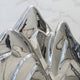 The Summit Abstract Steel Mountain Sculpture by Giant Sculptures features shiny, reflective silver peaks that mirror distorted images. Set against a white marble-like backdrop, its an ideal piece for modern mountain decor lovers.