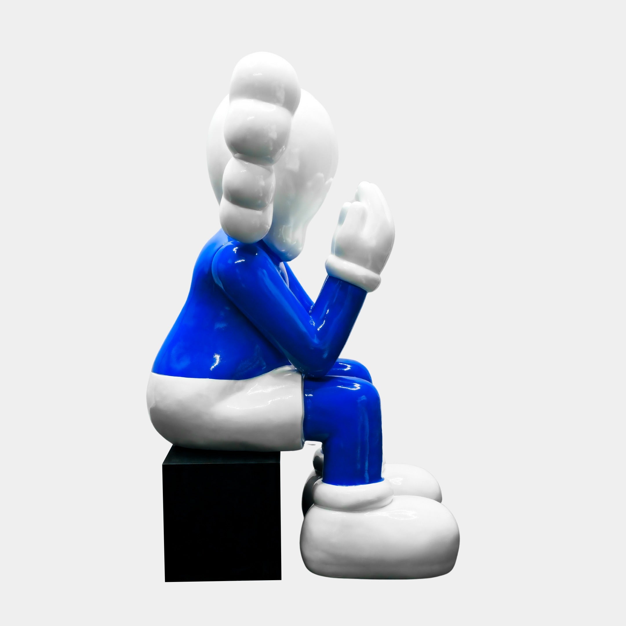 Giant Sculptures presents the Ex-Display White & Blue Iconify Melancholy Sitting Sculpture (130cm), featuring a cartoon character with a white face, blue body, and oversized white gloves and shoes. Sitting on a black cube and appearing deep in thought, it makes for a striking contemporary centerpiece.