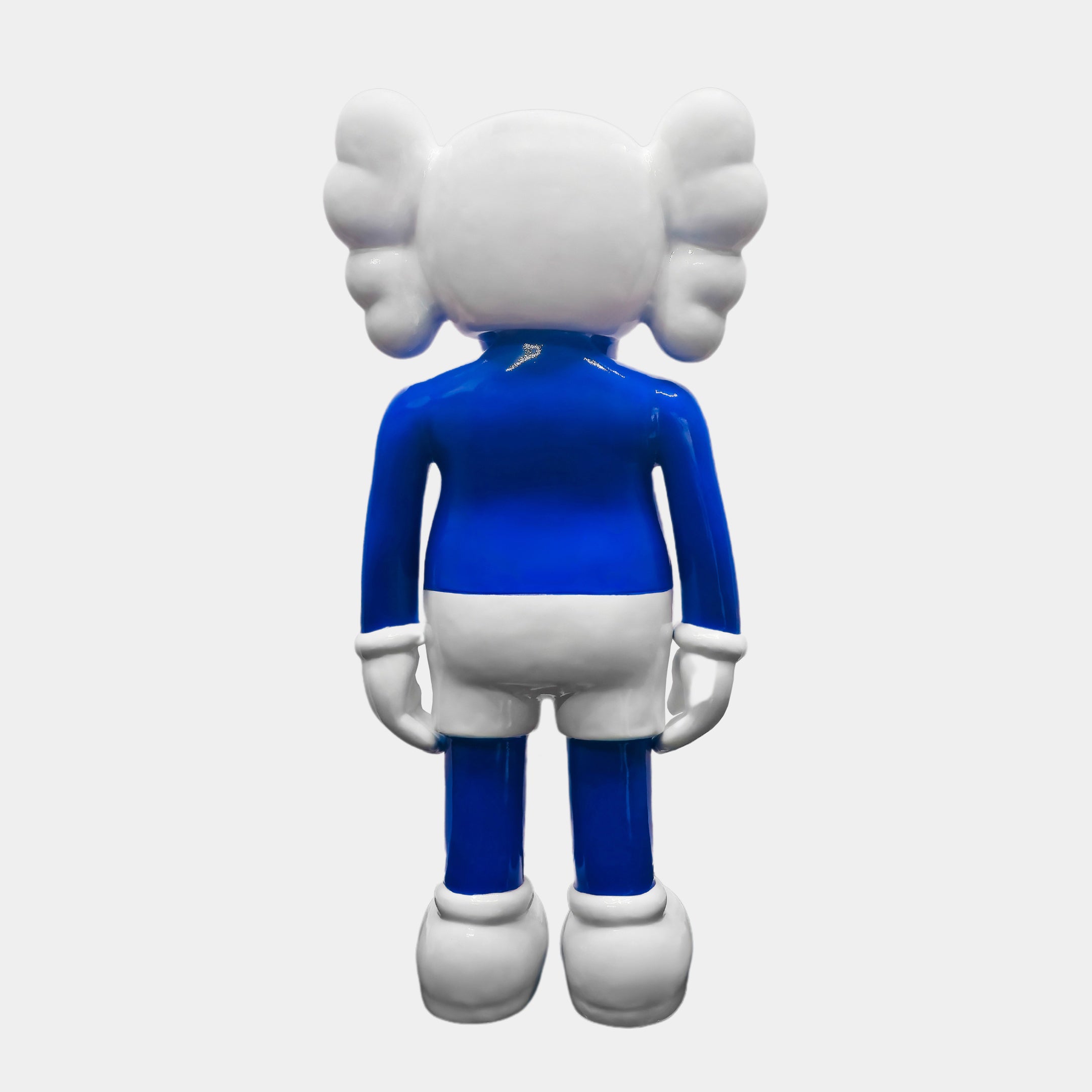 The Giant Sculptures Ex-Display Deep Blue Iconify Standing Sculpture features a modern design with a large, round head and wing-like ears. Standing 168cm tall, it wears a blue shirt, white shorts, matching gloves and shoes against a plain background, with its back turned to the viewer.