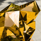 Close-up of the gold human sculpture's angular surfaces, showing how the golden reflections create a dynamic play of light on the metallic surface.