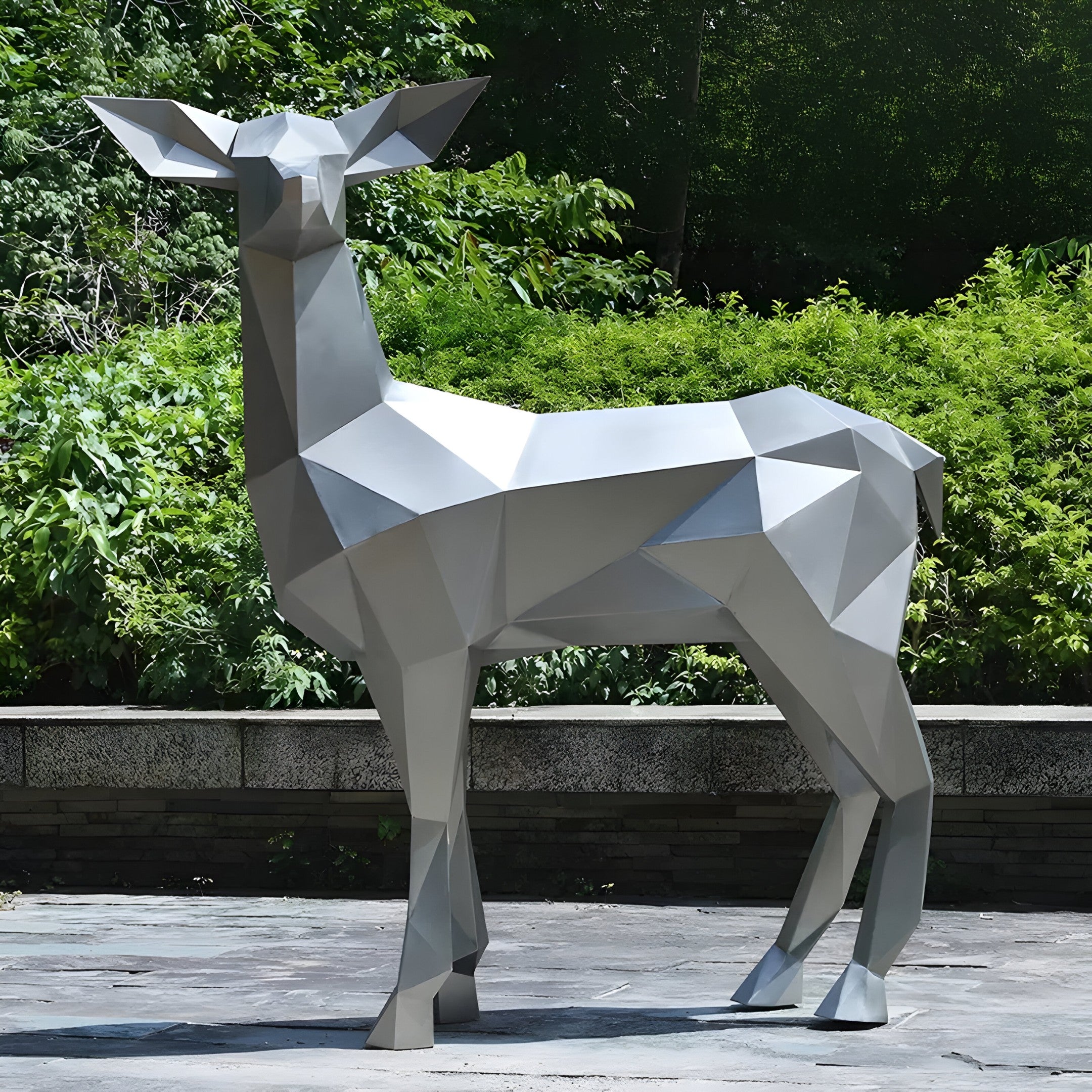 The "Deer II Geometric Steel Outdoor Sculpture - 160cm" by Giant Sculptures is positioned on a stone base amidst vibrant green vegetation. Its angular design lends a modern and abstract look to this outdoor artwork.