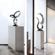 In a minimalist room with marble flooring, two abstract metal sculptures from Giant Sculptures stand elegantly on white pedestals. The first sculpture features intertwined loops of silver, while the second, named "Wings Of Light Silver Abstract Steel Sculpture - 102cm," showcases upward-curving, feather-like elements. Both pieces exude modern sophistication against a softly lit backdrop.