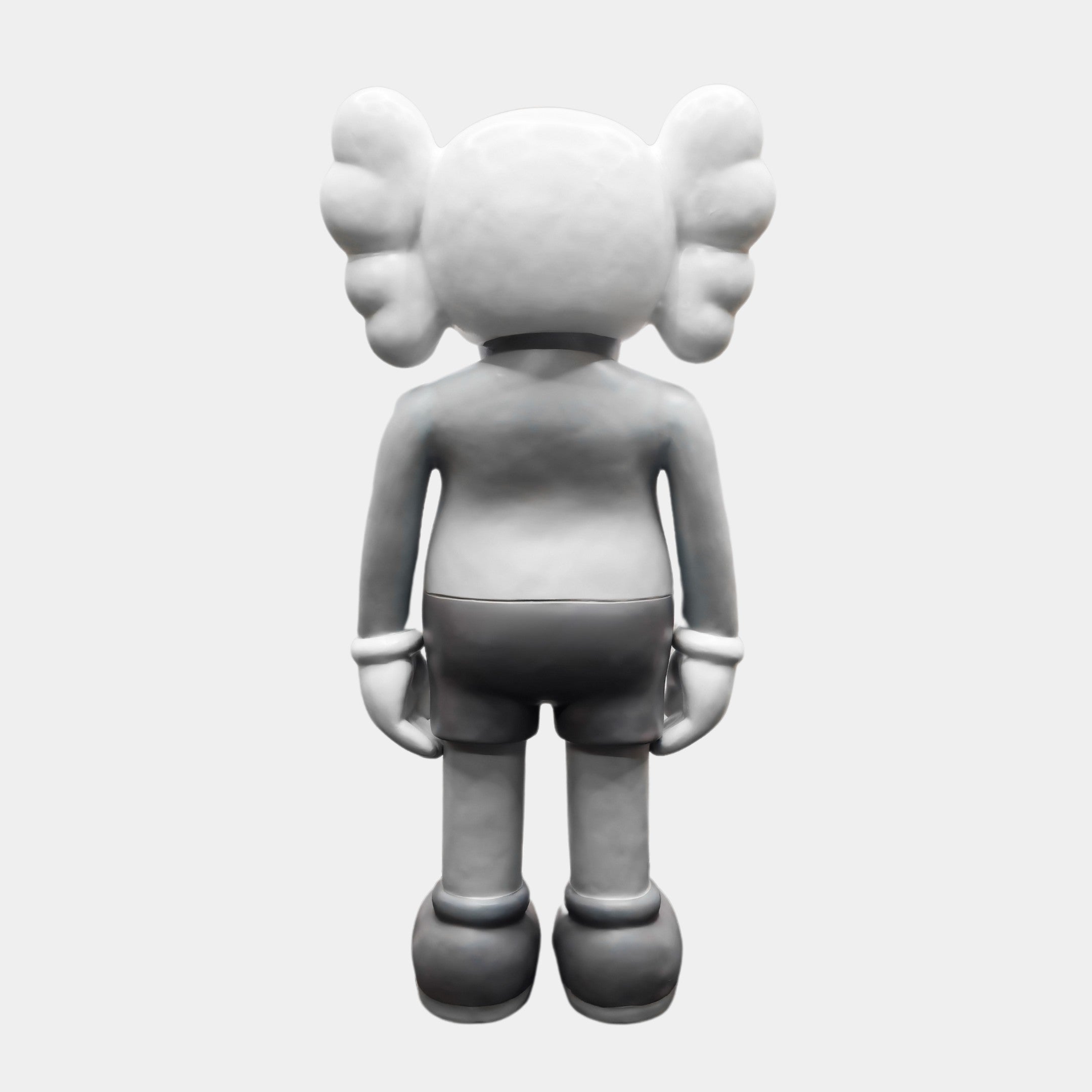 A monochrome figure with wing-like ears facing away, reminiscent of the Ex-Display Slay Grey Iconify Standing Sculpture by Giant Sculptures, has a smooth, stylized look wearing shorts and large shoes against a plain white backdrop.