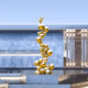 The Molecular Gold Organic Steel Outdoor Sculpture by Giant Sculptures stands 226cm tall, featuring shiny gold spheres in a twisting design set in a reflective pool. It complements the sleek lines and soft lighting of a contemporary building, creating an exquisite outdoor art display.