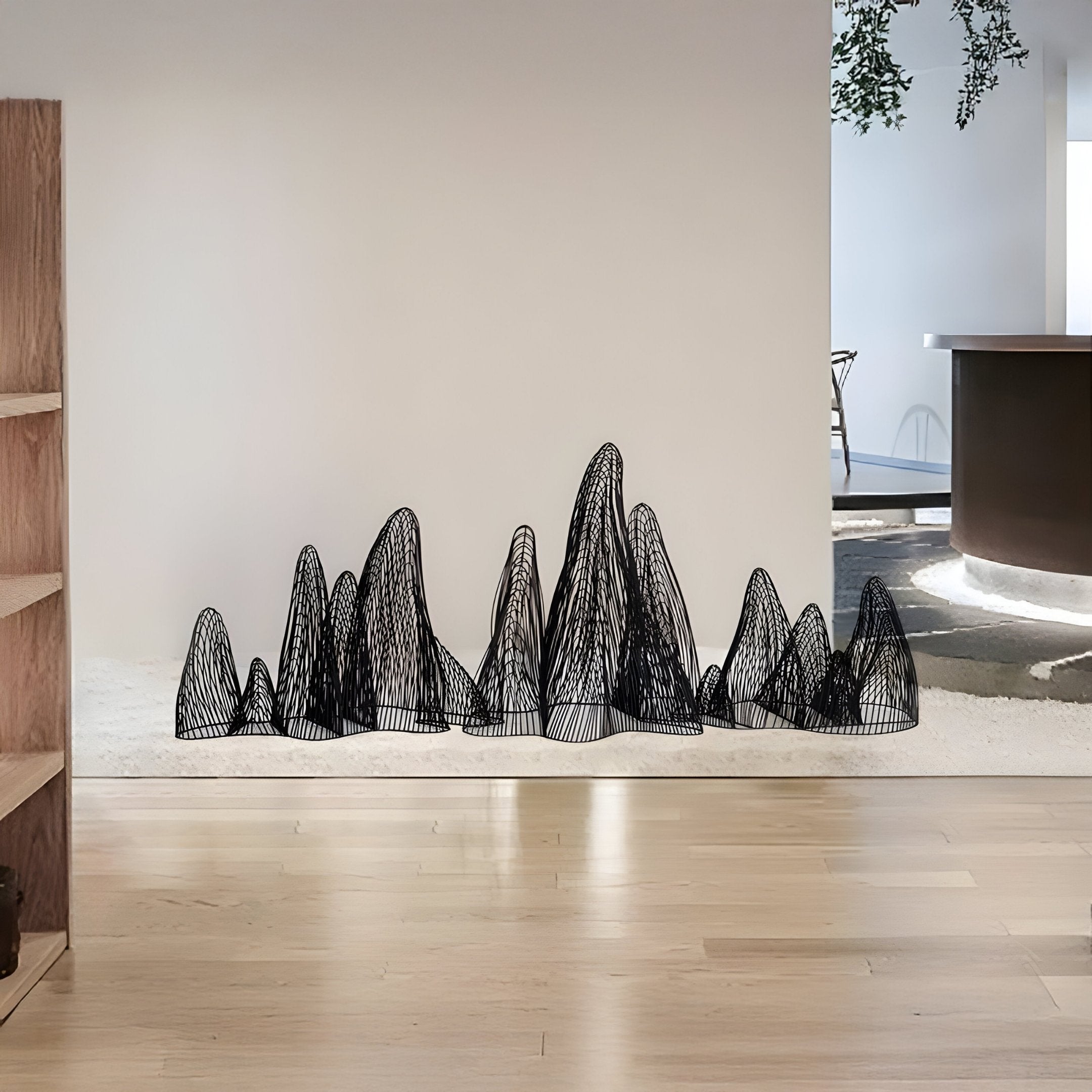 The Ascent Black Wireframe Steel Mountain Sculpture by Giant Sculptures features abstract geometric peaks in black wire mesh, resting on a white surface with light wood flooring, embodying contemporary design in a minimalistic indoor setting.