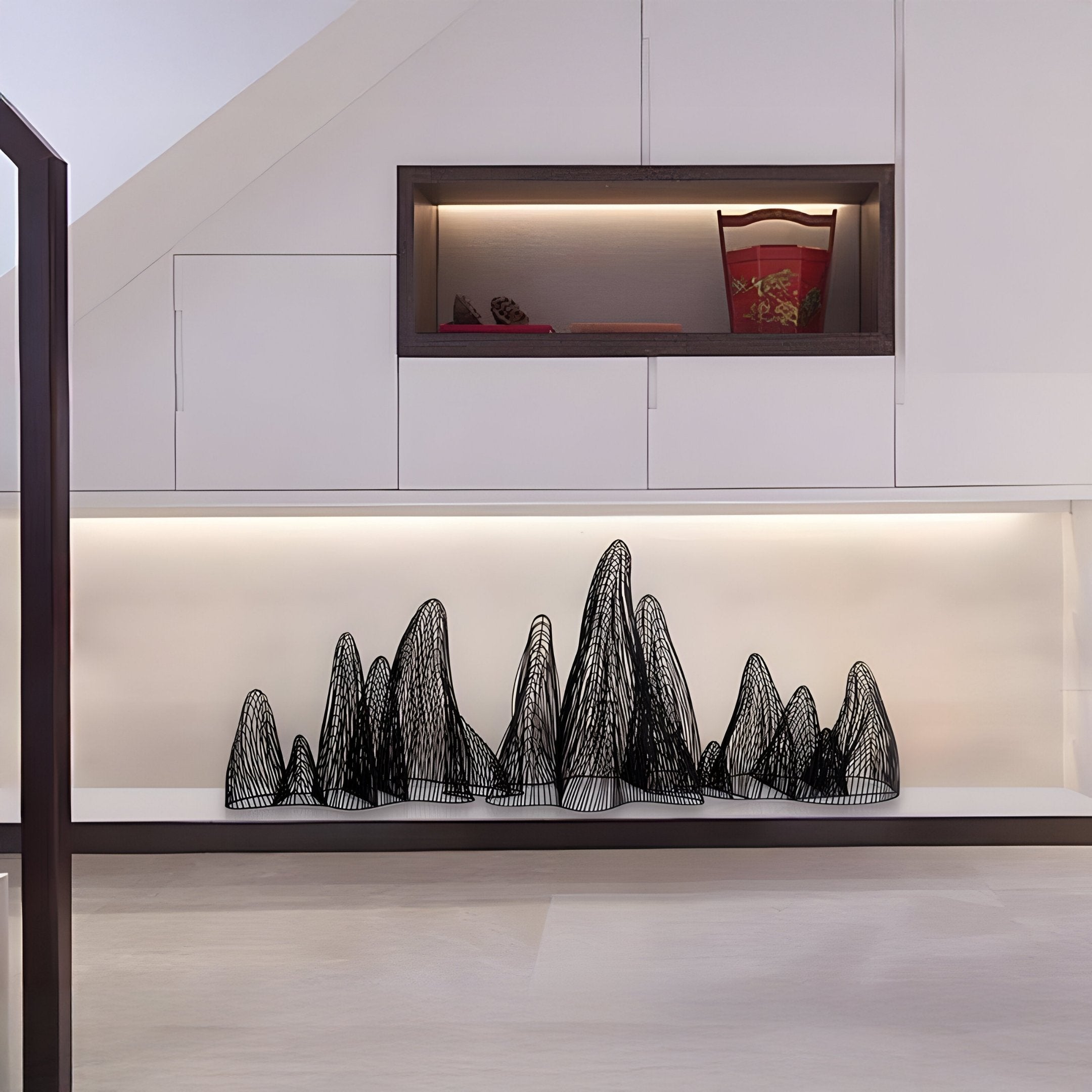 Sleek modern interior with white cabinets features a display shelf. Below it, the Ascent Black Wireframe Steel Mountain Sculpture from Giant Sculptures adds depth, while a soft, warm light highlights the minimalist design enhanced by stainless steel accents.