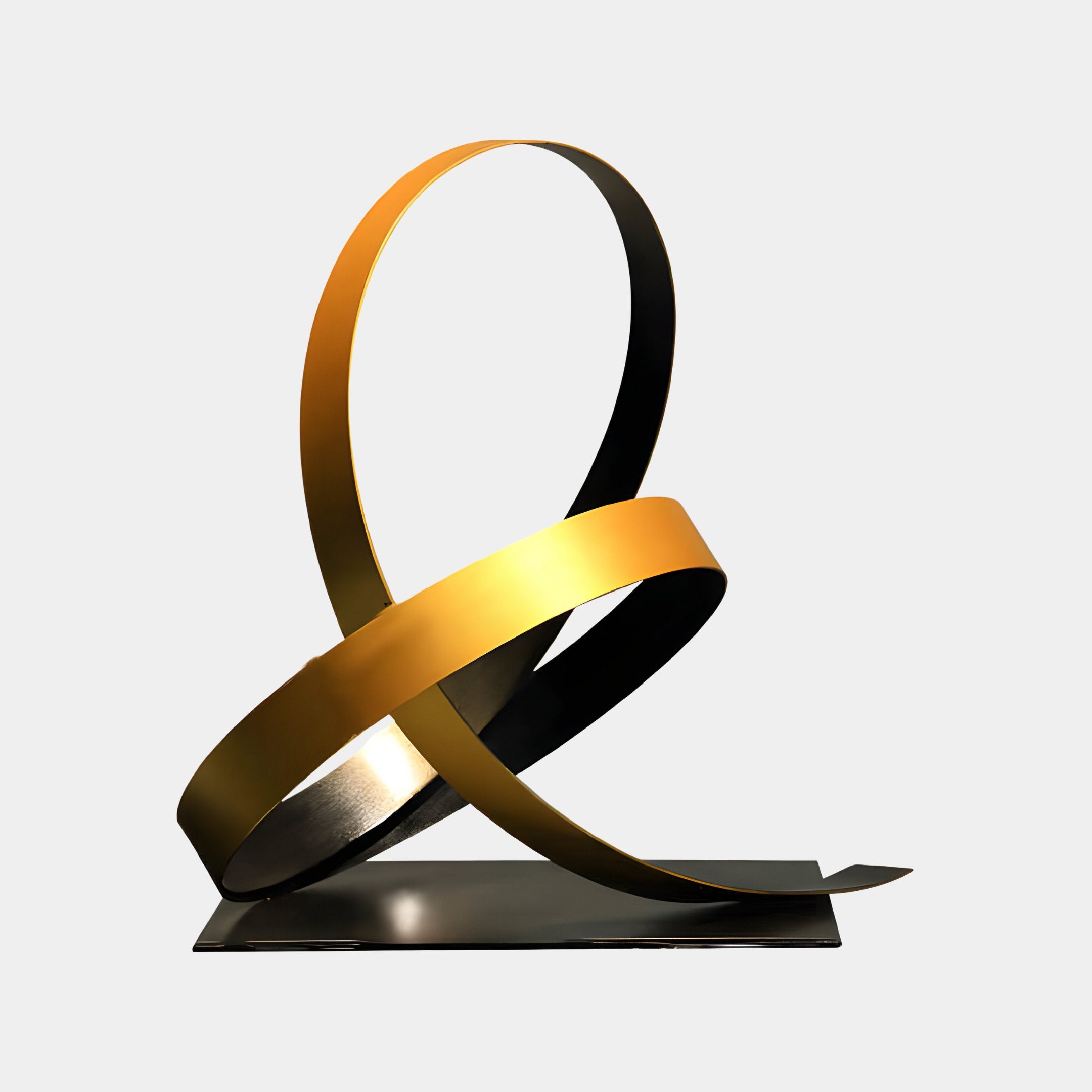 The Ribbon Gold II Abstract Steel Sculpture by Giant Sculptures showcases a contemporary design with two interlocking metallic ribbons, one in gold and the other in black, gracefully positioned on a flat rectangular base. This 56cm artwork presents a fluid, looped appearance against a simple white backdrop, epitomizing the sophistication of a gold ribbon sculpture.