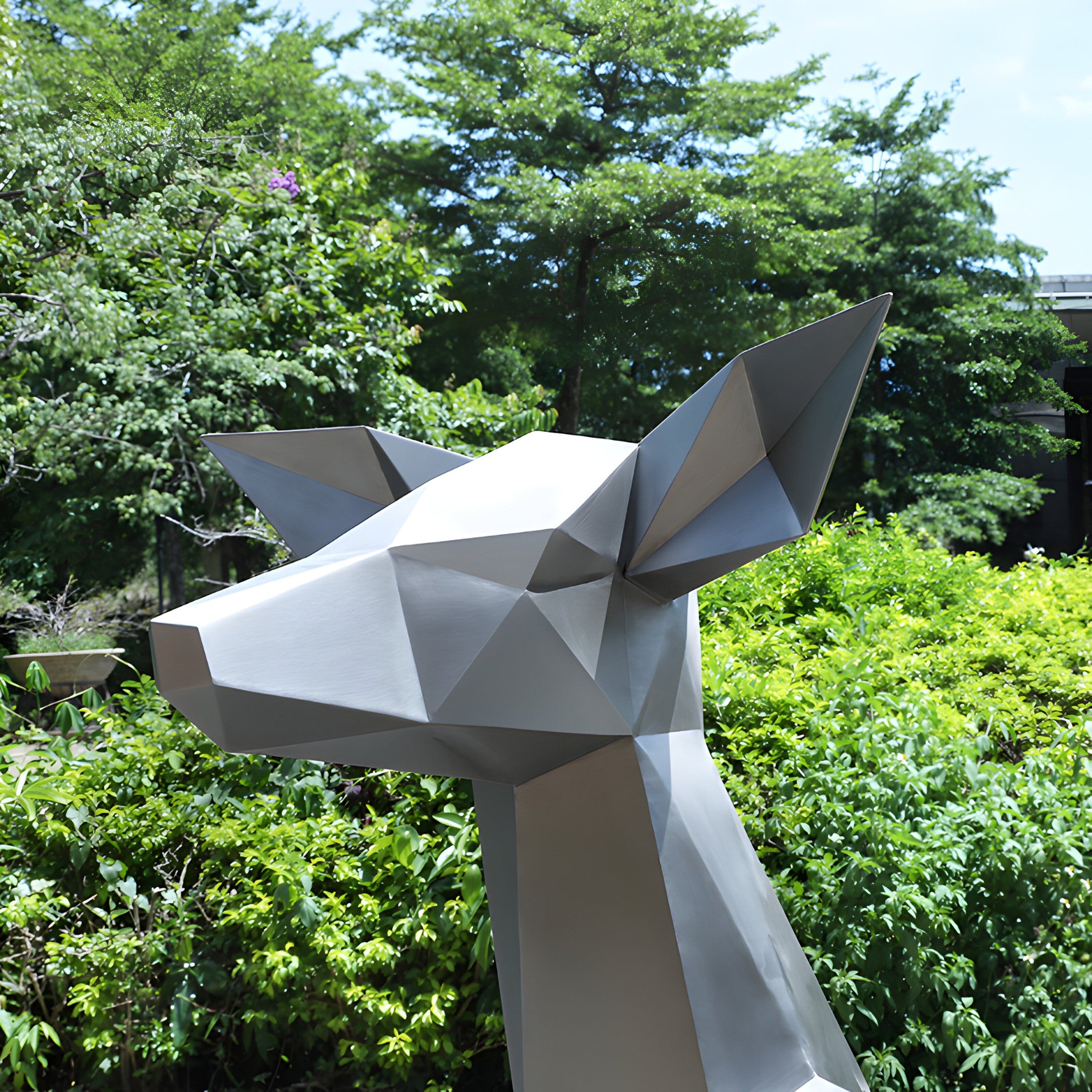 The Deer III Geometric Steel Outdoor Sculpture by Giant Sculptures, measuring 120cm, stands against a backdrop of lush green foliage and trees under a clear blue sky.