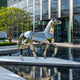  Full view of the geometric horse sculpture near a modern architectural building with large glass windows and a reflective pond, showing the dynamic pose and angles of the sculpture.