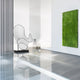 In a modern, minimalist room with glossy floors and sleek white walls featuring vertical stripes, a large wire abstract chair takes center stage. To the right, vibrant green grass-like wall art enhances the Giant Sculptures Cheri Silver Abstract Steel Sculpture - 72cm.